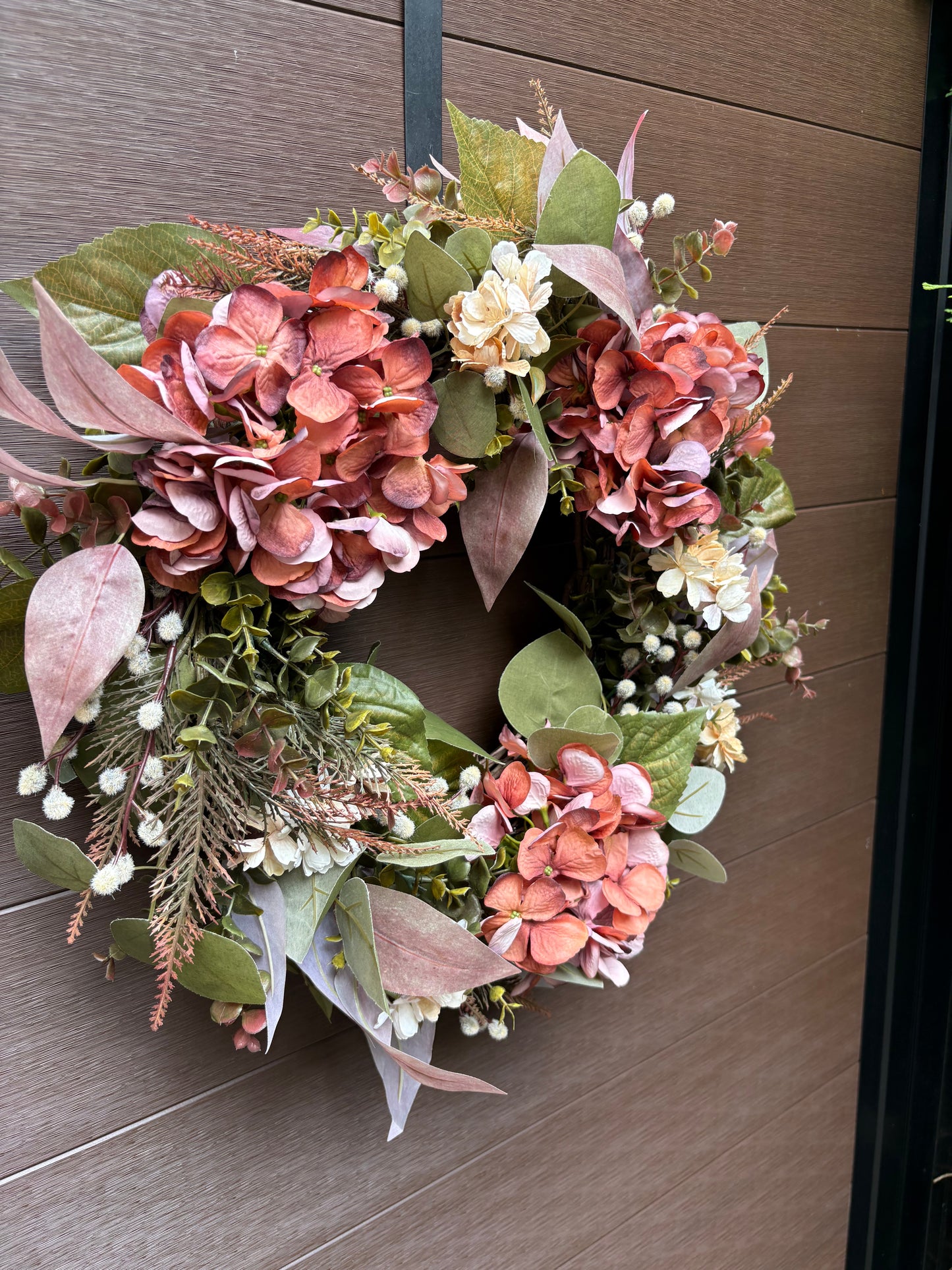 Couronne d’automne avec hortensias artificiels roses, fleurs crème et feuillages verts.