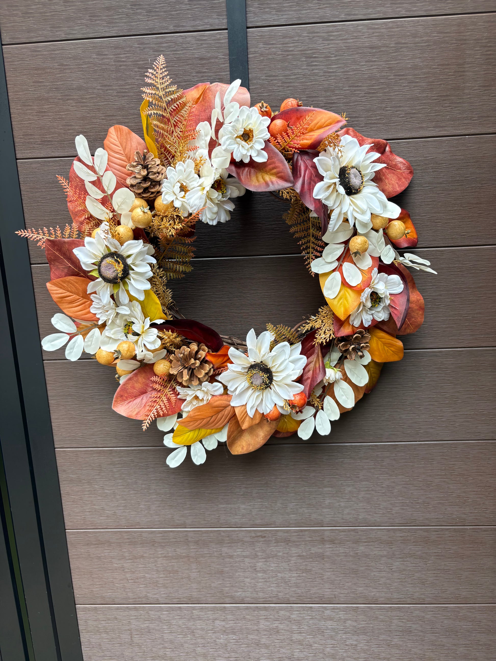 Couronne automnale garnie de fleurs blanches, fougères et feuillages rouille