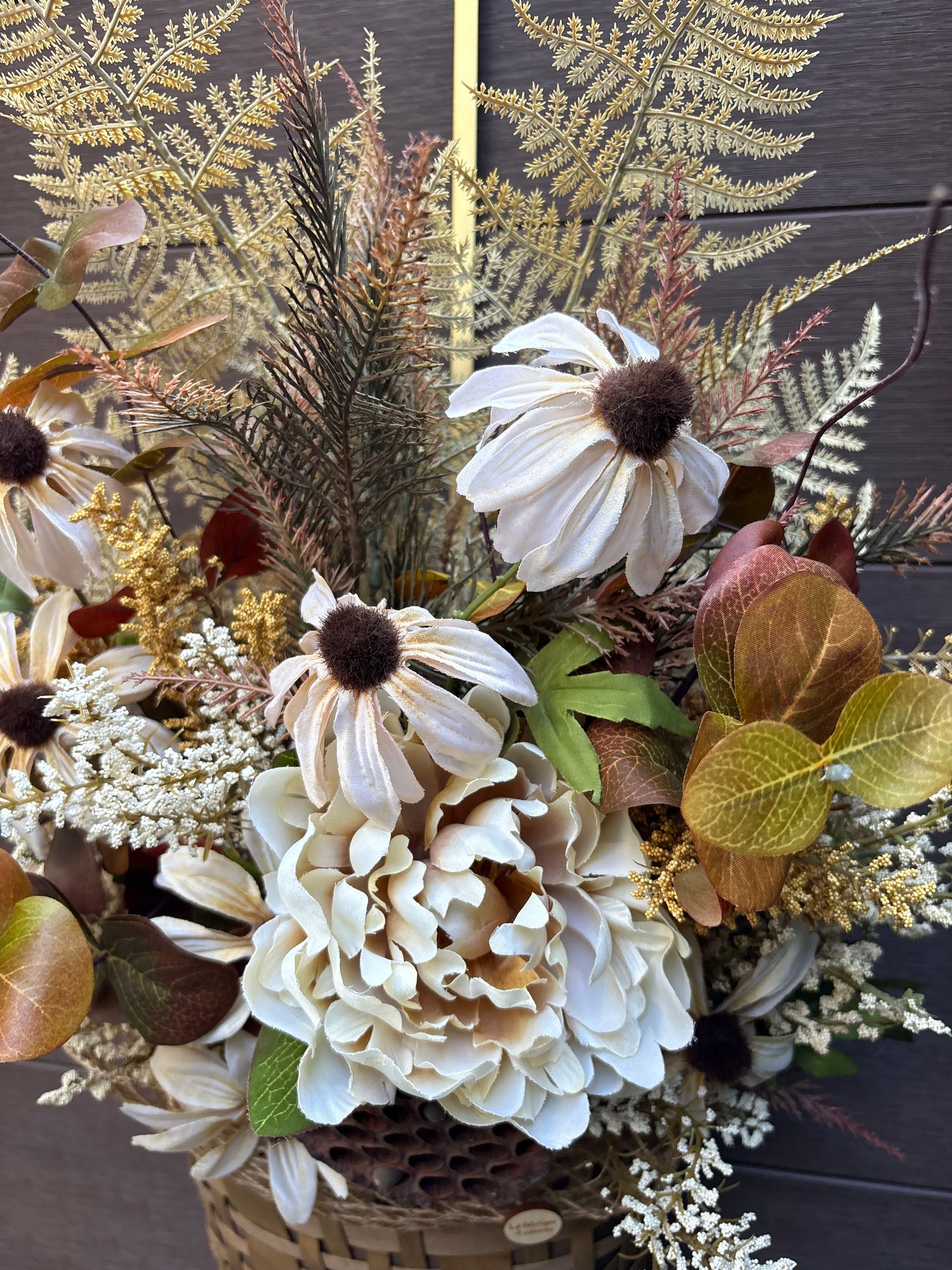 Détail des fleurs crème et des feuillages naturels du panier mural.
