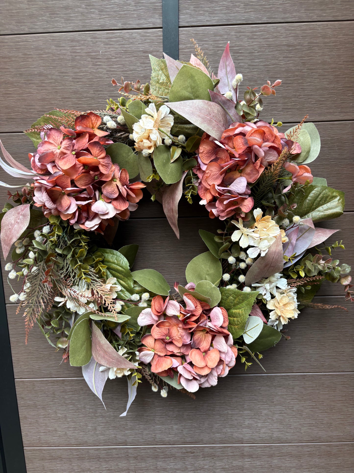 Couronne florale rose et corail présentée sur un mur brun
