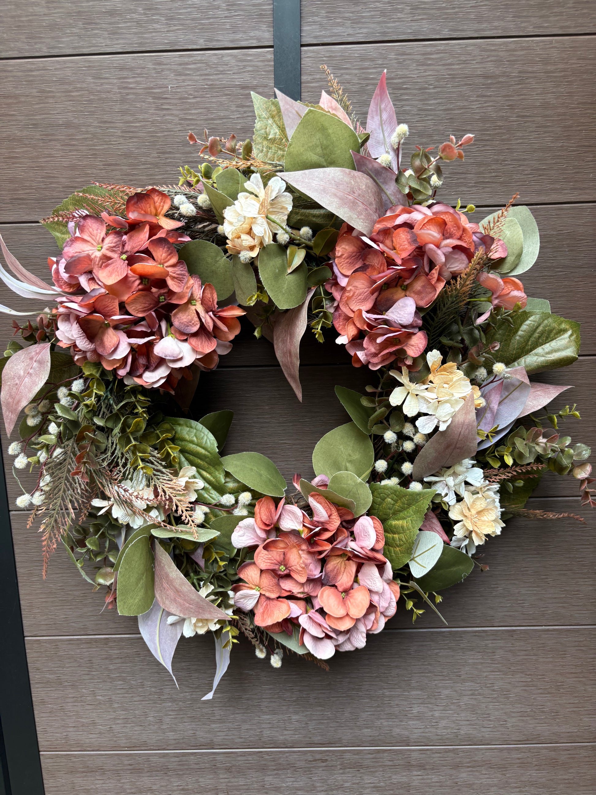 Couronne florale rose et corail présentée sur un mur brun