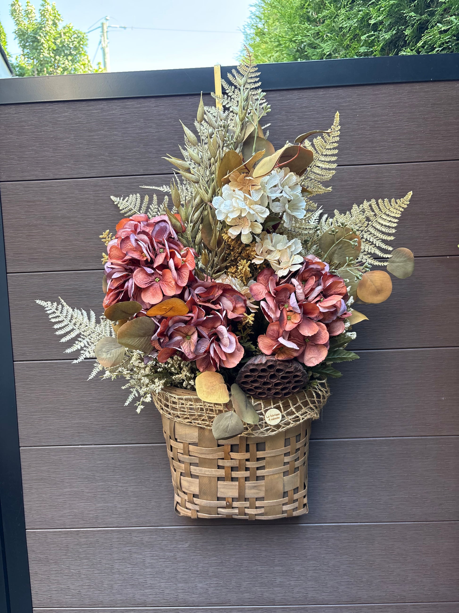 Panier mural d’automne en osier avec hortensias bordeaux, fleurs crème et feuillages naturels