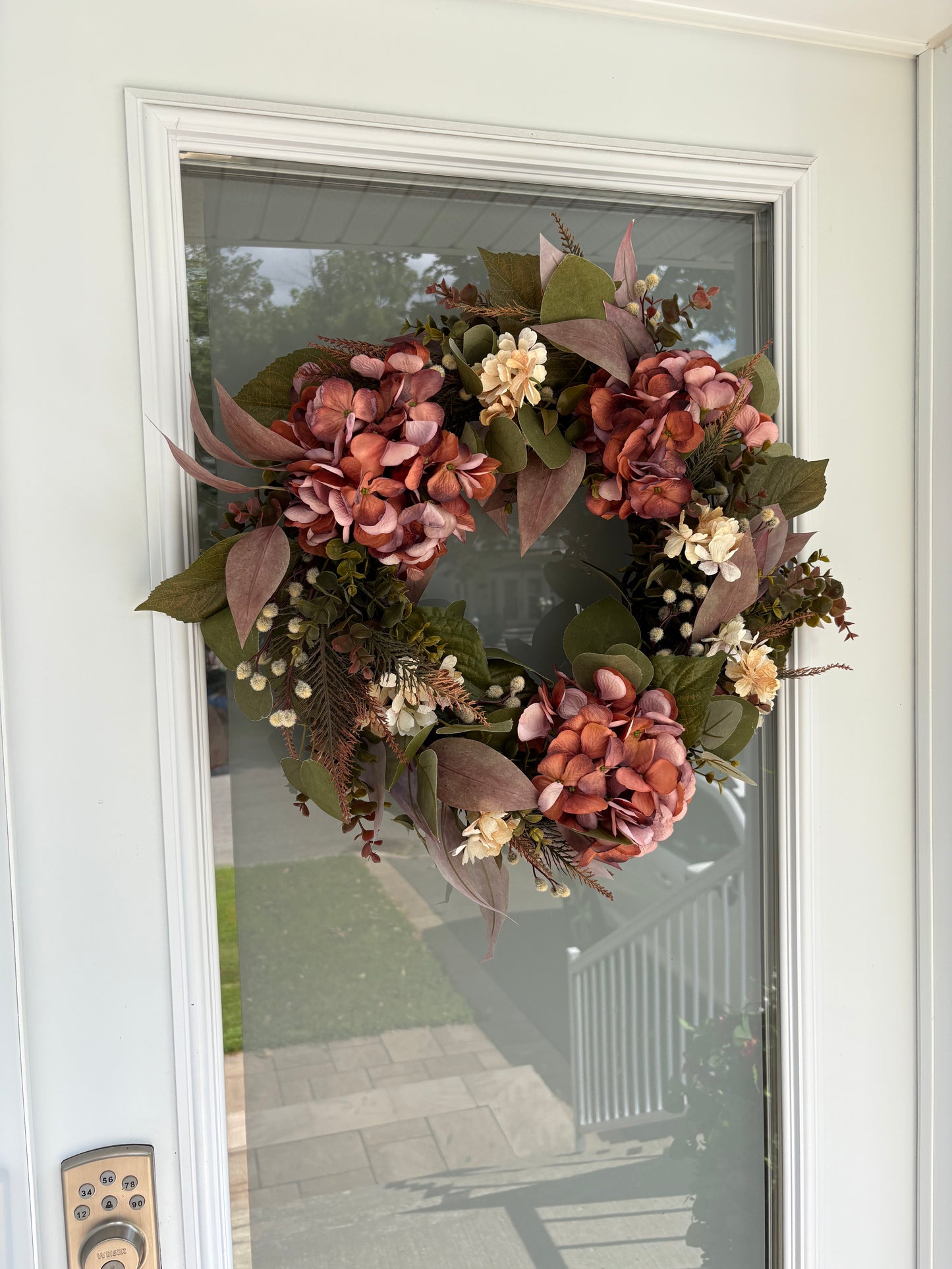 Couronne d’automne installée sur une porte d’entrée blanche.