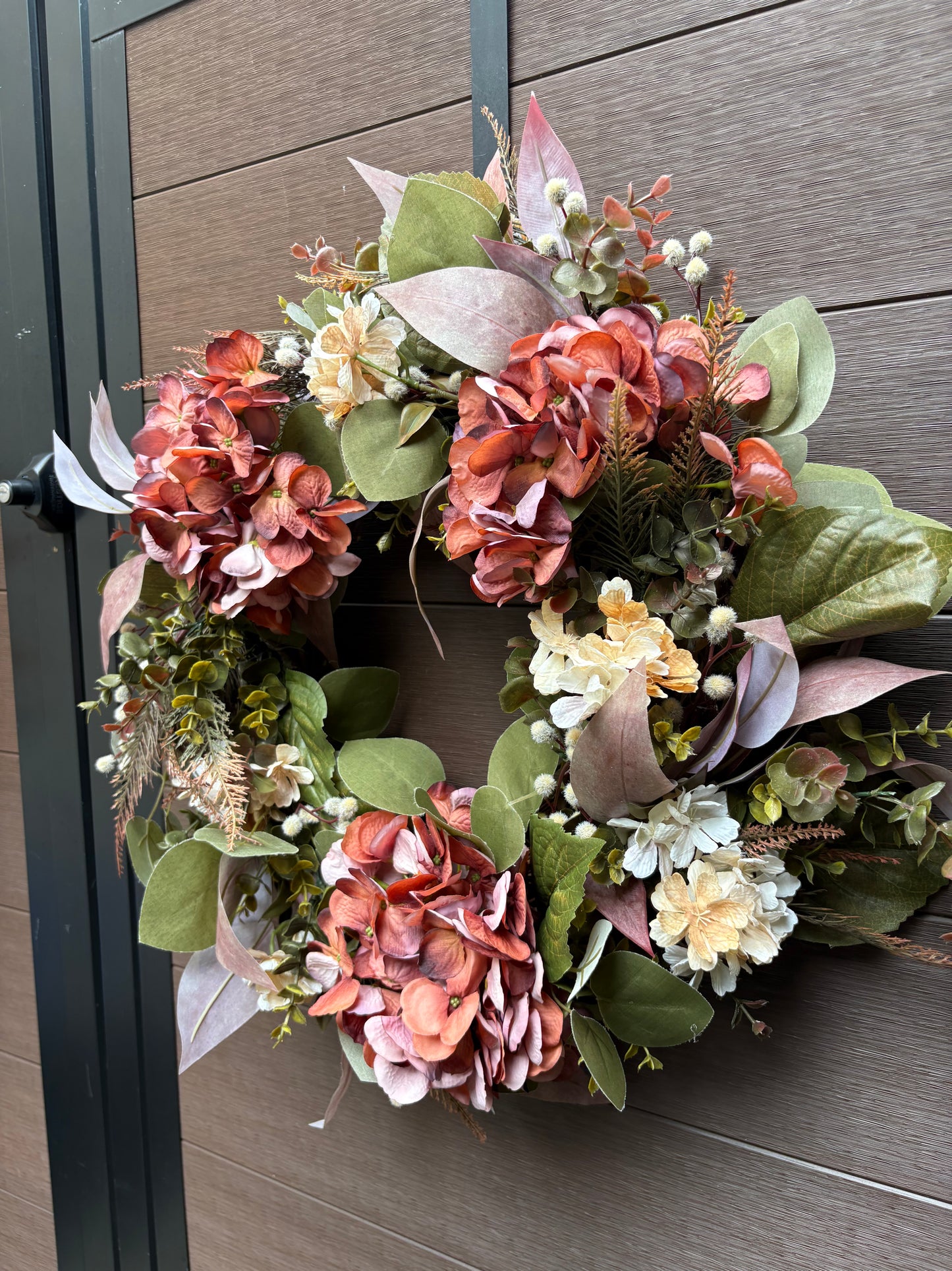 Vue de face de la couronne florale d’automne rose et corail sur mur brun.
