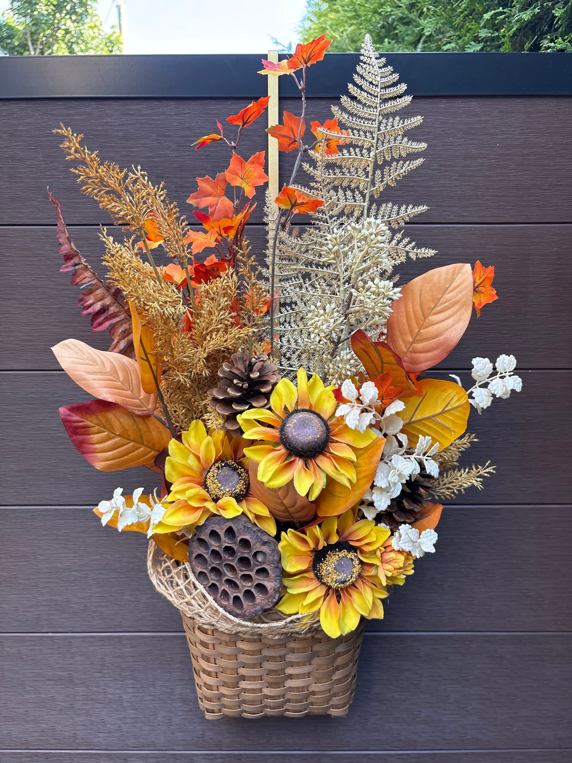 Panier mural d’automne en osier avec tournesols dorés, feuillages orangés et fougères